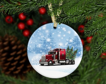 May include: A red semi-truck hauling a Christmas tree through a snowy winter landscape. The truck is decorated with lights and the tree is adorned with ornaments. This is a round ceramic ornament.