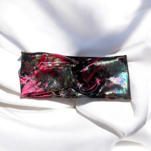Può includere: Un cerchietto iridiscente rosa, nero e oro con un design annodato.