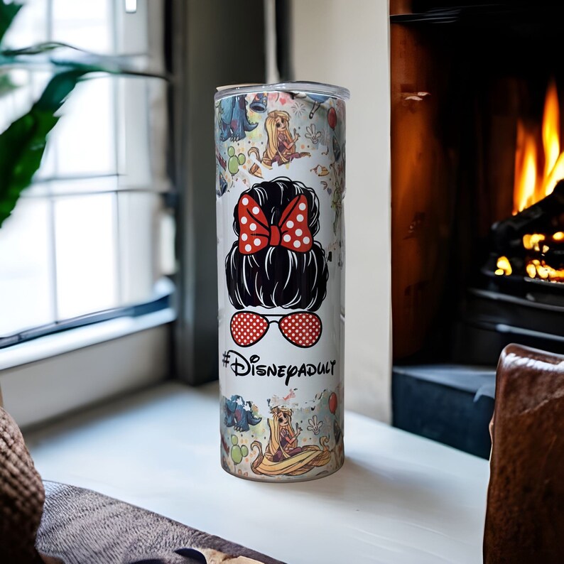 May include: White stainless steel tumbler with a colorful print of Disney characters and the text "#DisneyAdult". The tumbler features a red bow and sunglasses.