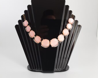 May include: A pink statement necklace with large round stones on a black display stand.