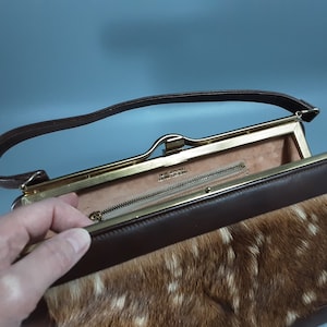 May include: A brown leather purse with a gold clasp and a fur lining. The purse has a long strap and a small zippered pocket inside.
