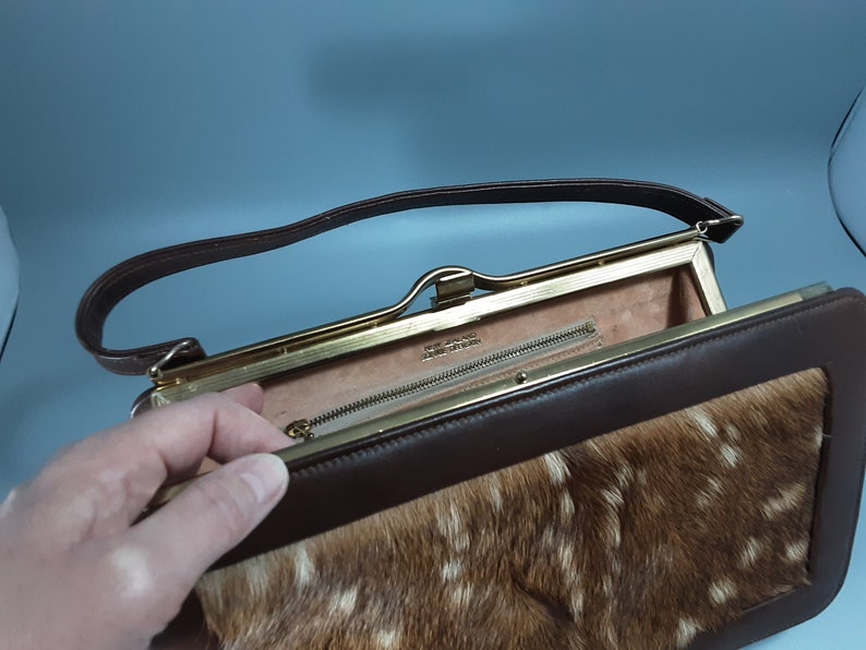 May include: A brown leather purse with a gold clasp and a fur lining. The purse has a long strap and a small zippered pocket inside.