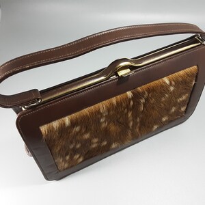 May include: A brown leather handbag with a gold clasp and a patch of brown and white fur on the front.