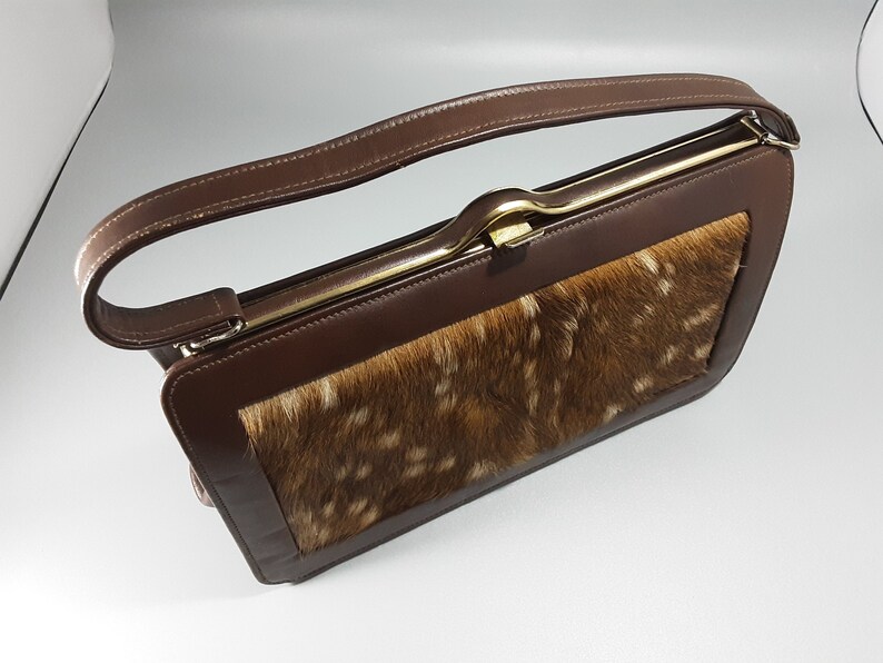 May include: A brown leather handbag with a gold clasp and a patch of brown and white fur on the front.