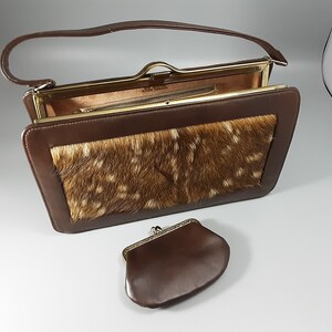 May include: A brown leather purse with a flap closure and a gold-tone frame. The purse has a deer skin patch on the front and a matching brown leather coin purse.