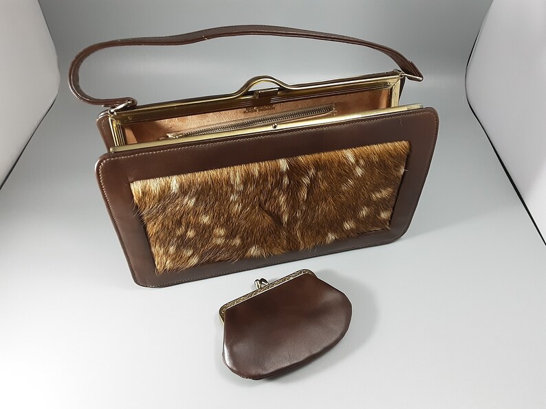 May include: A brown leather purse with a flap closure and a gold-tone frame. The purse has a deer skin patch on the front and a matching brown leather coin purse.