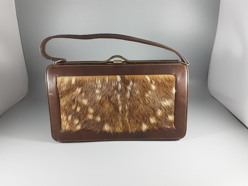 May include: A brown leather handbag with a flap closure and a top handle. The flap is made of a brown and white spotted fur.