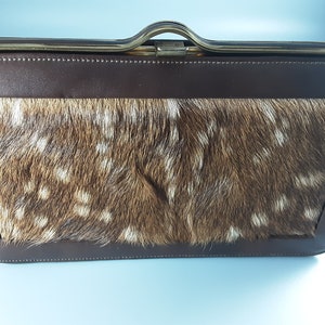 May include: A brown leather purse with a flap closure and a gold metal frame. The purse is lined with a brown and white spotted fur.