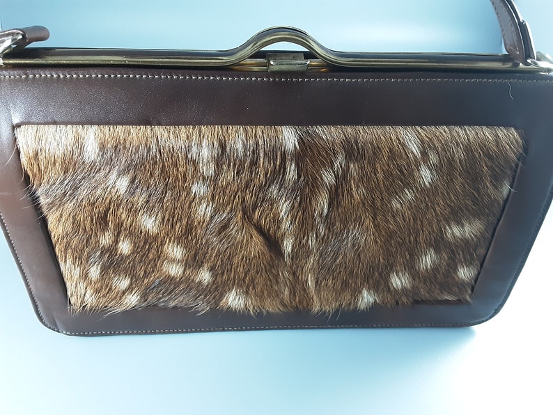 May include: A brown leather purse with a flap closure and a gold metal frame. The purse is lined with a brown and white spotted fur.
