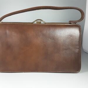 May include: A brown leather handbag with a gold clasp and a single top handle.