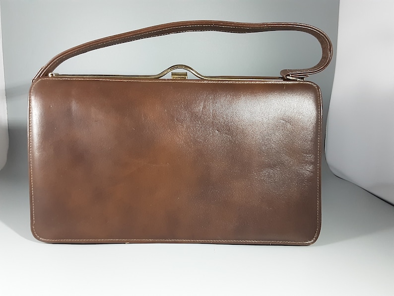 May include: A brown leather handbag with a gold clasp and a single top handle.