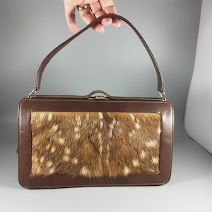 May include: A brown leather handbag with a top flap closure and a  deer skin panel. The bag has a single top handle.