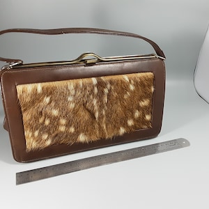 May include: A brown leather handbag with a flap closure and a top handle. The flap is made of a spotted fawn fur.