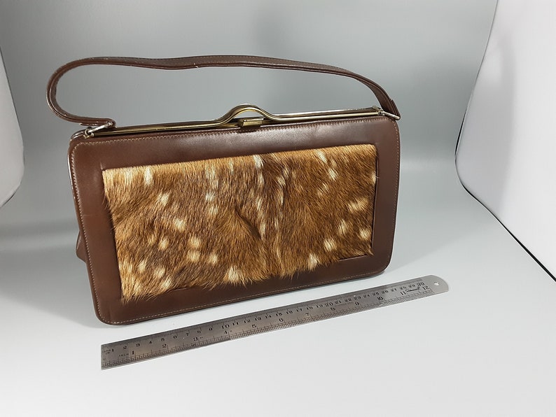 May include: A brown leather handbag with a flap closure and a top handle. The flap is made of a spotted fawn fur.