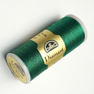 May include: A spool of green Diamant embroidery thread by DMC. The spool is labeled with the DMC logo and the text "Diamant".