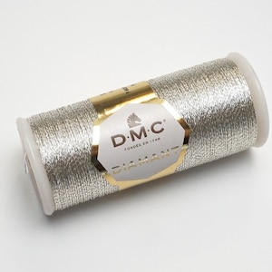 May include: A silver metallic thread spool with a gold label that reads "D.M.C.  FONDÉE EN 1790  DIAMANT".