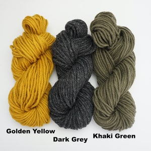 Puede incluir: Tres ovillos de hilo en amarillo dorado, gris oscuro y verde caqui.