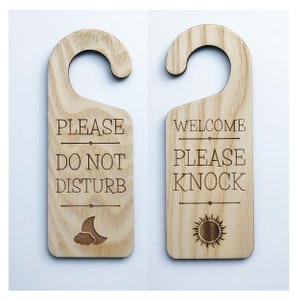 May include: Two wooden door hangers with engraved text. The left hanger says "Please Do Not Disturb" with a moon and cloud design. The right hanger says "Welcome Please Knock" with a sun design.