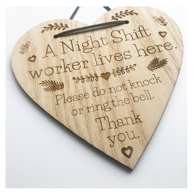May include: A wooden heart-shaped sign with the text "A Night Shift worker lives here. Please do not knock or ring the bell. Thank you." The sign has a black string for hanging.