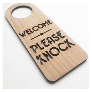May include: Wooden door hanger with the text "Welcome" and "Please Knock" in a black font.