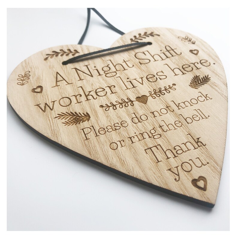 May include: A wooden heart-shaped sign with the text "A Night Shift worker lives here. Please do not knock or ring the bell. Thank you." The sign has a distressed wood finish and is decorated with small hearts and floral designs.