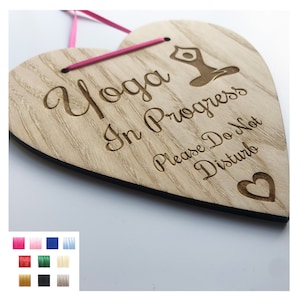 May include: Wooden heart-shaped sign with the text "Yoga in Progress Please Do Not Disturb" and a small heart cutout. The sign is hanging from a pink ribbon.