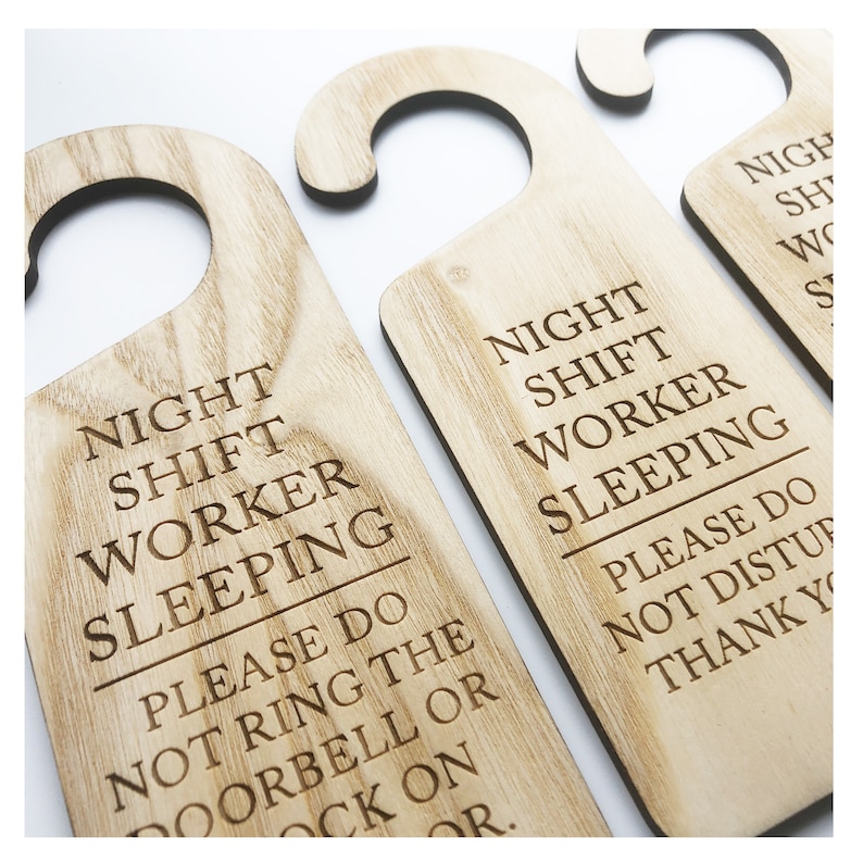 Może przedstawiać: Trzy drewniane wieszaki na drzwi z tekstem "Night Shift Worker Sleeping. Please do not ring the doorbell or knock on the door." Wieszaki są jasnobrązowe z naturalnym usłojeniem drewna.