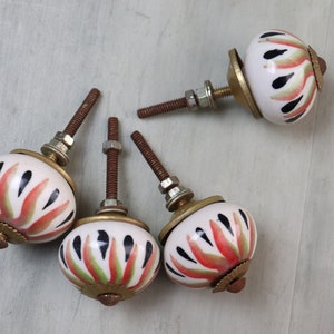 May include: Four white ceramic cabinet knobs with a floral design in shades of red, green, and black. Each knob has a gold-colored base and a screw.