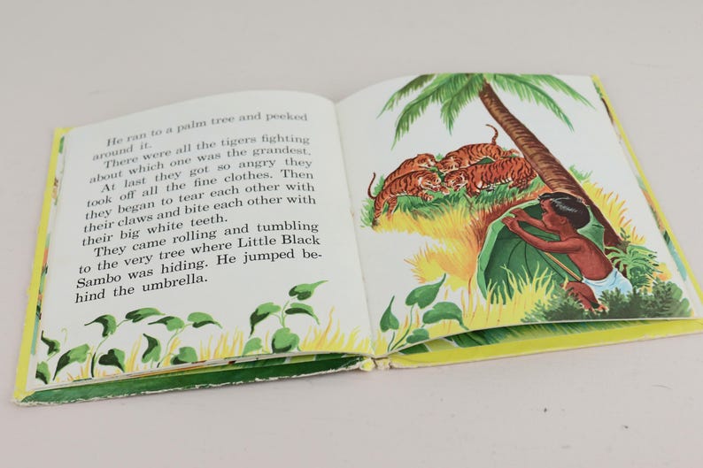 May include: An open book with illustrations. The right-hand page depicts a boy hiding under a leaf, with tigers and a palm tree. The left page contains text. The book has a yellow border.