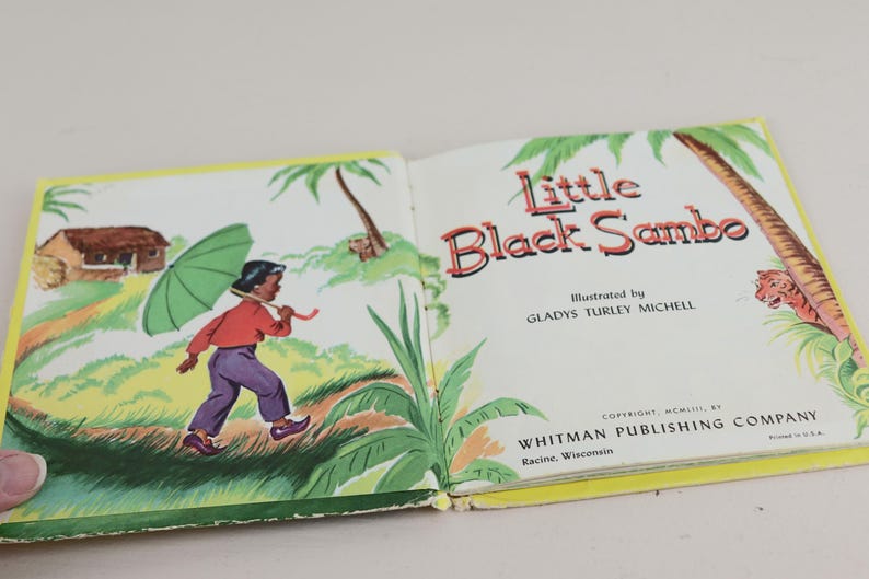 May include: Open book titled "Little Black Sambo" with illustrations. The left page shows a child with an umbrella, the right page has text and a tiger illustration. Published by Whitman Publishing Company.