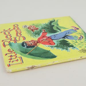 May include: A vintage children's book titled "Little Black Sambo" with a yellow cover. The cover features an illustration of a boy with an umbrella, set against a green and yellow background. The book shows signs of wear.