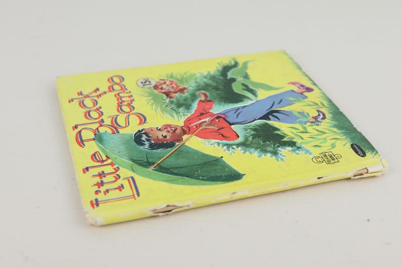May include: A vintage children's book titled "Little Black Sambo" with a yellow cover. The cover features an illustration of a boy with an umbrella, set against a green and yellow background. The book shows signs of wear.