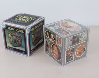 May include: A vintage Photo Cube with a box. The box is white, blue, and black with the words "PHOTO CUBE" in yellow. The cube is clear with photos on each side. The photos are of people and scenes.