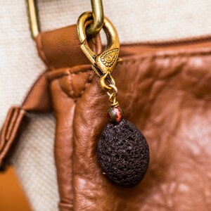 May include: A brown leather bag with a gold clasp and a black lava rock charm.