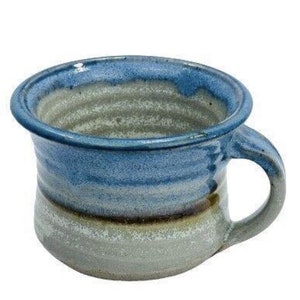 May include: A handmade ceramic mug with a blue, brown, and white glaze. The mug has a wide, rounded base and a handle.