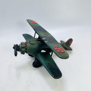 May include: A vintage green biplane toy with red insignia on the wings and tail. The propeller is black, and the plane shows signs of wear, suggesting it is an antique or a well-loved item. The biplane is a classic toy.