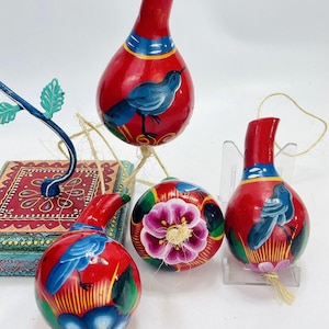 May include: Four hand-painted gourd ornaments with a red base and colorful designs. Each ornament features a bird, a flower, and intricate details. The ornaments are strung with twine and ready to hang.