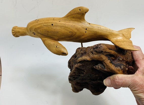 A hand-carved wooden dolphin with a literal bottle for a nose — folk-art craftsmanship meets a groan-worthy pun, mounted on burl wood like a tiny museum piece.
