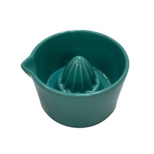 May include: A teal ceramic citrus juicer with a built-in reamer and a pouring spout. The juicer has a conical reamer in the center and a wide bowl for catching juice. The design is simple and functional for kitchen use.