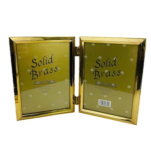 May include: A hinged, solid brass photo frame. The frame is gold-colored and features the text "Solid Brass PHOTO FRAME" in a decorative font. Each frame holds a 5" x 7" photo. The frame is hand polished and lacquered.
