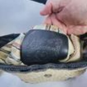 May include: A black handbag featuring a cream-colored interior lining with a subtle plaid pattern. The bag includes a black leather patch embossed with the brand name Brighton, positioned centrally within the open main compartment.