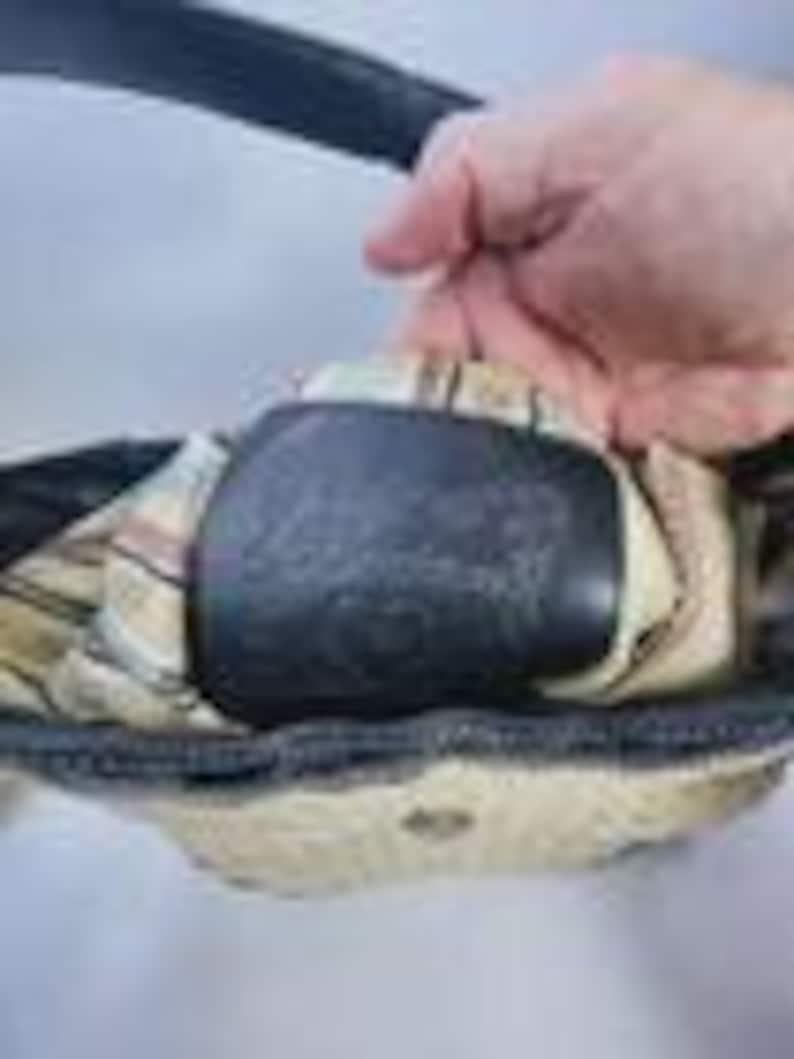 May include: A black handbag featuring a cream-colored interior lining with a subtle plaid pattern. The bag includes a black leather patch embossed with the brand name Brighton, positioned centrally within the open main compartment.