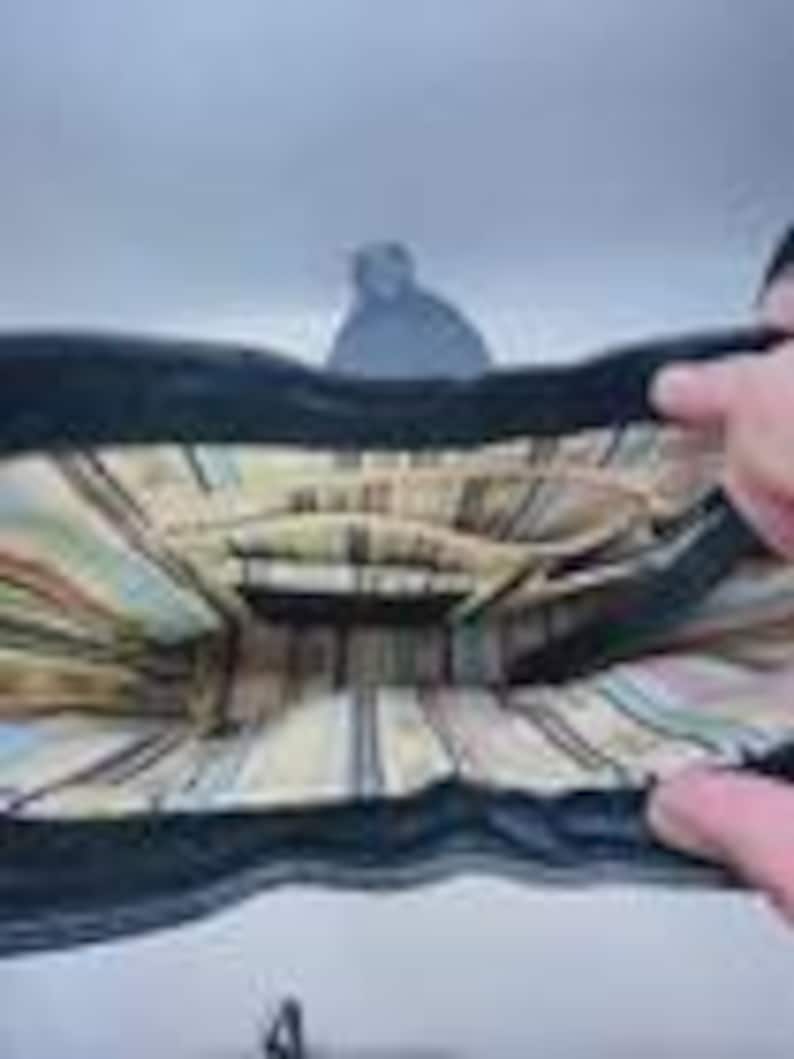 May include: The interior of a black handbag featuring a beige lining with a vertical striped pattern in shades of brown, blue, and white. The bag includes a central zippered compartment and open side pockets for organization within the main space.