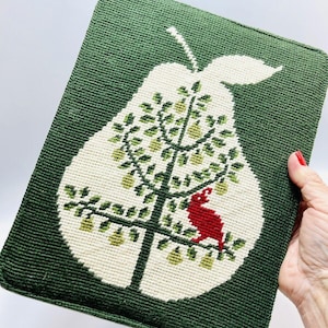 May include: A green needlepoint pillow with a white pear design. The pear is filled with small green pears and a red bird sits on a branch.
