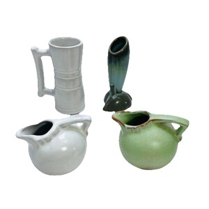 May include: Four ceramic pitchers and vases in various shapes and colors. Includes a tall, light gray mug with a handle, a white pitcher with a handle, a green pitcher with a handle, and a dark green vase.