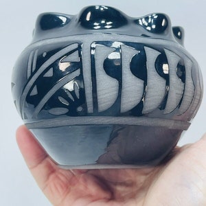 May include: A small, black pottery bowl with a gray and black geometric design. The bowl has a slightly rounded shape and a textured surface.