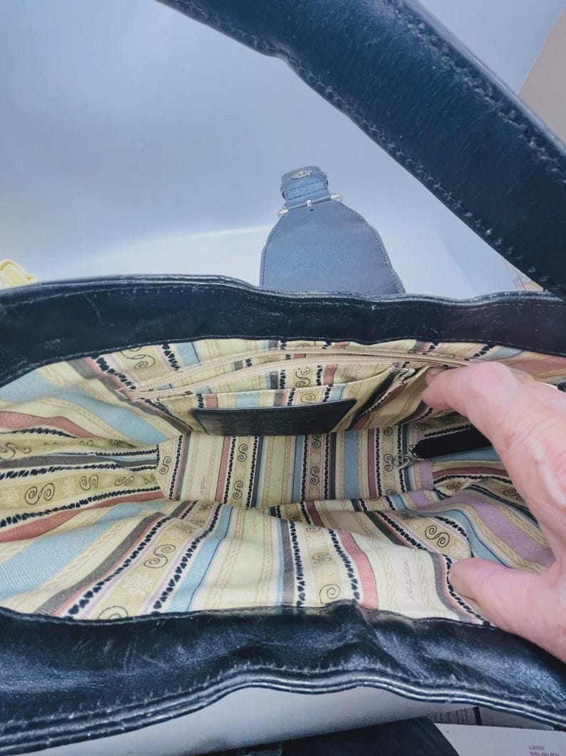 May include: A black leather handbag with a wide strap and a magnetic snap closure. The interior is lined with a cream-colored fabric featuring vertical stripes in light blue, pink, and brown, along with a repeating black swirl pattern.
