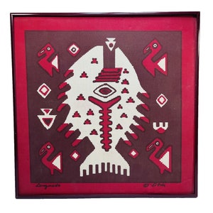 May include: A framed artwork with a geometric design in red, white, and brown. The design features a stylized bird and a central figure with a large eye. The artwork is signed "Longueado" and "J.C.Eris".