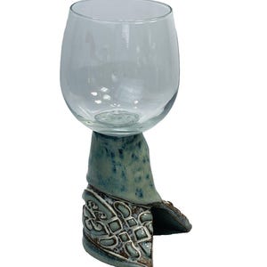 May include: A clear glass wine glass sits atop a hand-crafted ceramic base. The base is decorated with a blue and white glaze and intricate patterns.