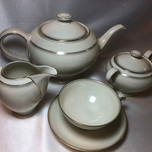 May include: A white tea set with gold trim. The set includes a teapot, creamer, sugar bowl, and a cup and saucer.